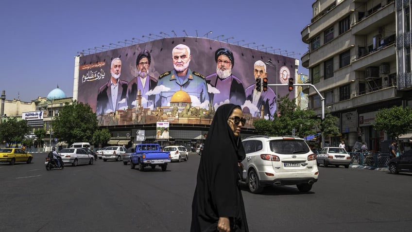 People move past a large banner featuring portraits of slain leaders from Iran-aligned armed groups, including Hamas leader Yahya Sinwar, Hezbollah leader Hassan Nasrallah, and Iranian commander Qasem Soleimani, in central Tehran, Iran, on May 1, 2025. 