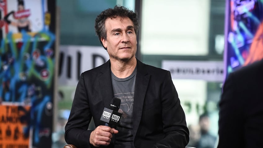 Doug LIman sitting in a chair holding a microphone