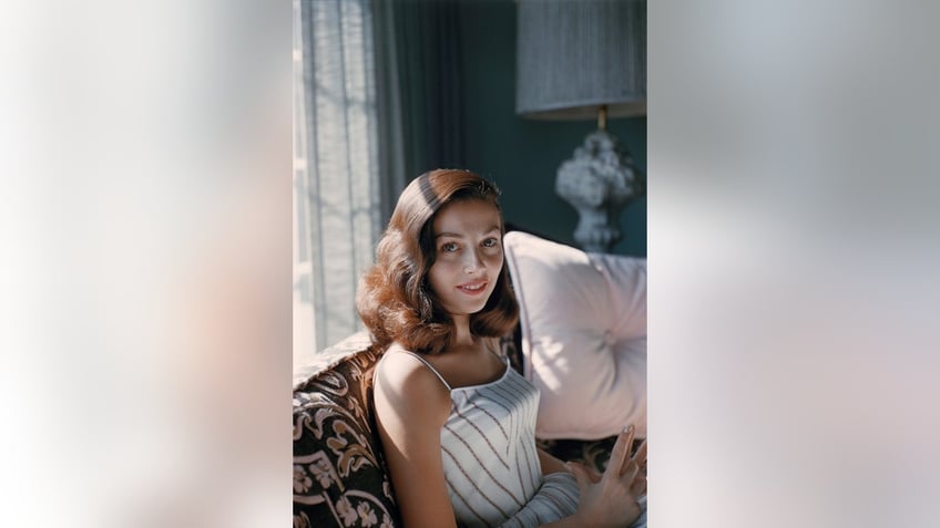 Pier Angeli in a spaghetti strapped white dress sitting on a couch