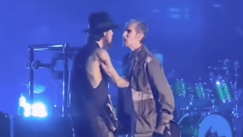 Dave Navarro with his back partially to the camera has a heated exchange with band member Perry Farrell, who leans into Dave