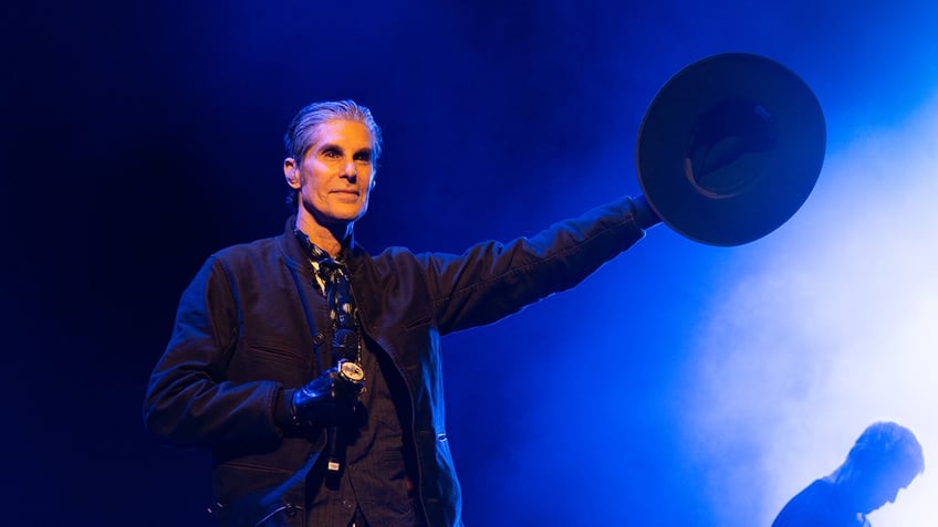 Perry Farrell standing on stage holding out hat