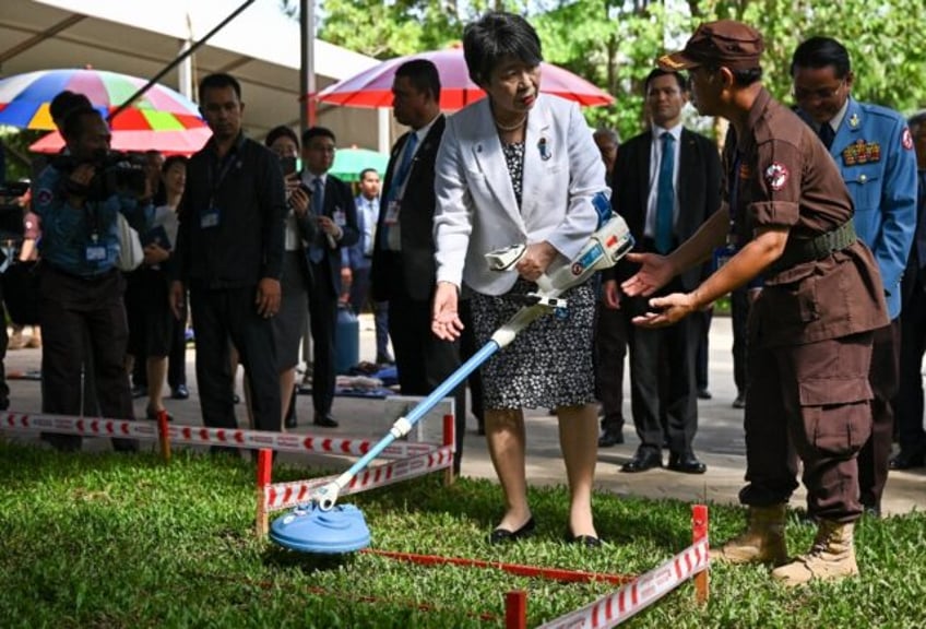 Japan's Foreign Minister Yoko Kamikawa (C) holds a mine detector and speaks to a deminer (