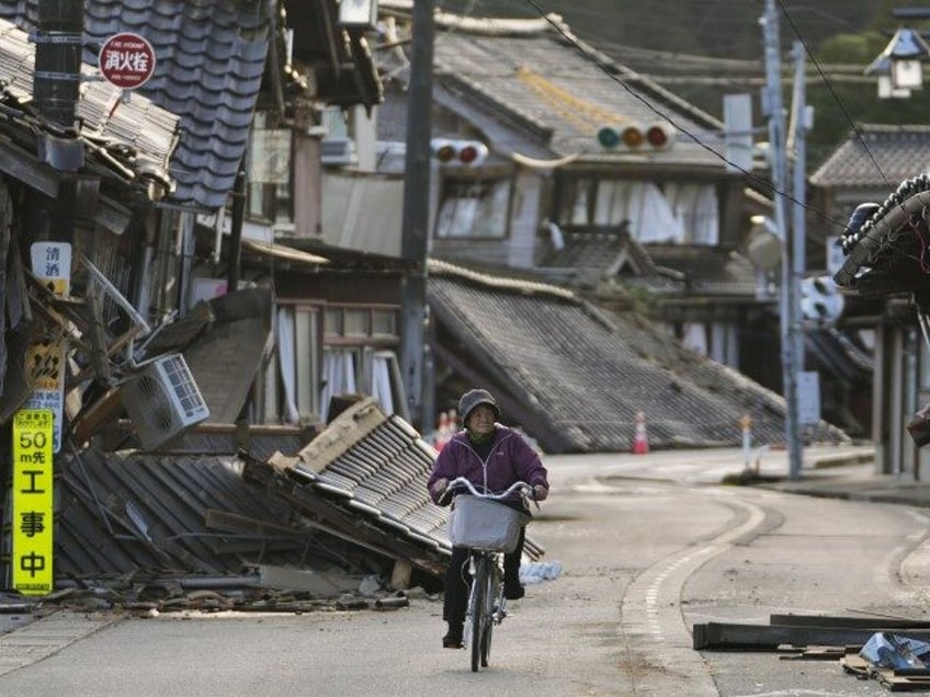 A woman bikes amid damaged houses in Noto town in the Noto peninsula facing the Sea of Japan, northwest of Tokyo, Tuesday, Jan. 2, 2024, following Monday's deadly earthquake. A series of powerful earthquakes that hit western Japan have damaged thousands of buildings, vehicles and boats. Officials warned that more …