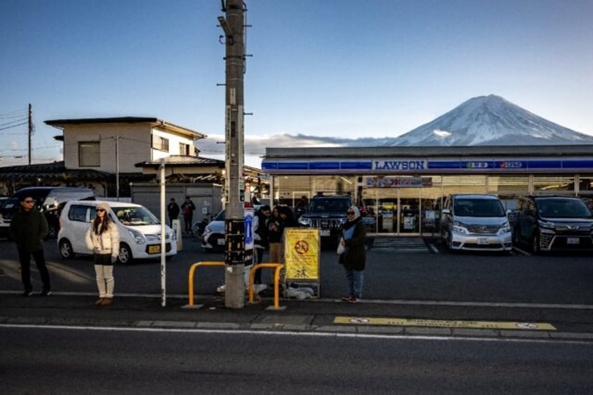 Tourists pose in front of a convenience store with Mount Fuji in the background, in the to