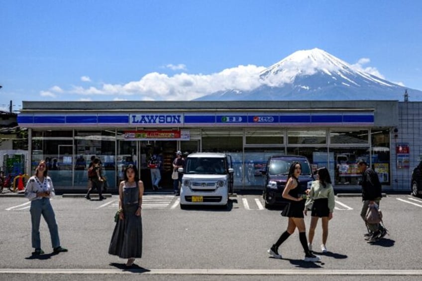Tourists pose in front of a convenience store with Mount Fuji on May 3, 2024, before a hug