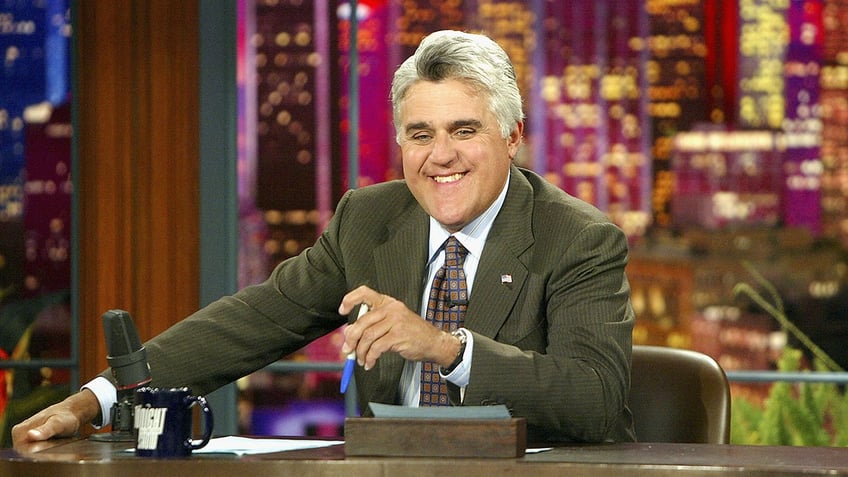 Jay Leno sitting behind the desk on the set of the Tonight Show