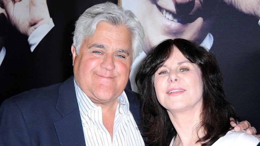 Jay Leno in a blue blazer smiles on the carpet with wife Mavis