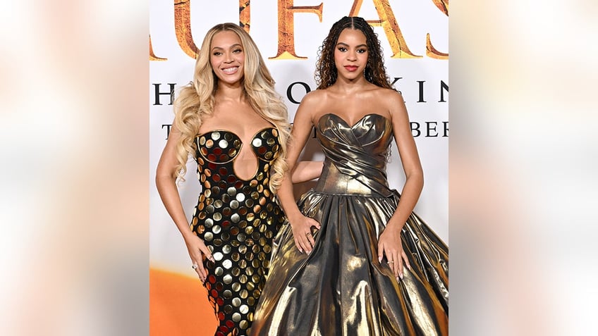 Beyoncé in a gold circle plunging dress smiles next to daughter Blue Ivy in a gold strapless dress at 'Mufasa: The Lion King' premiere