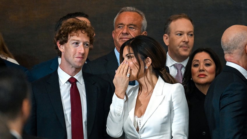 Lauren Sanchez whispering something to Mark Zuckerberg as he grins.