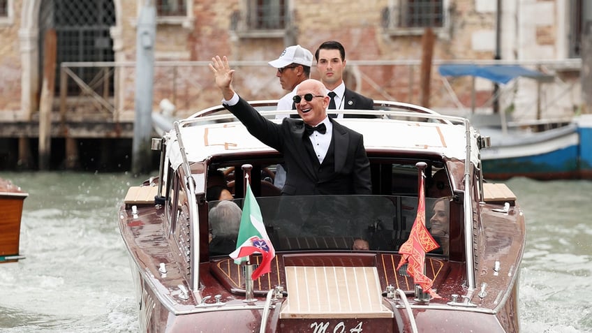 Jeff Bezos waving on a water taxi in a black tuxedo