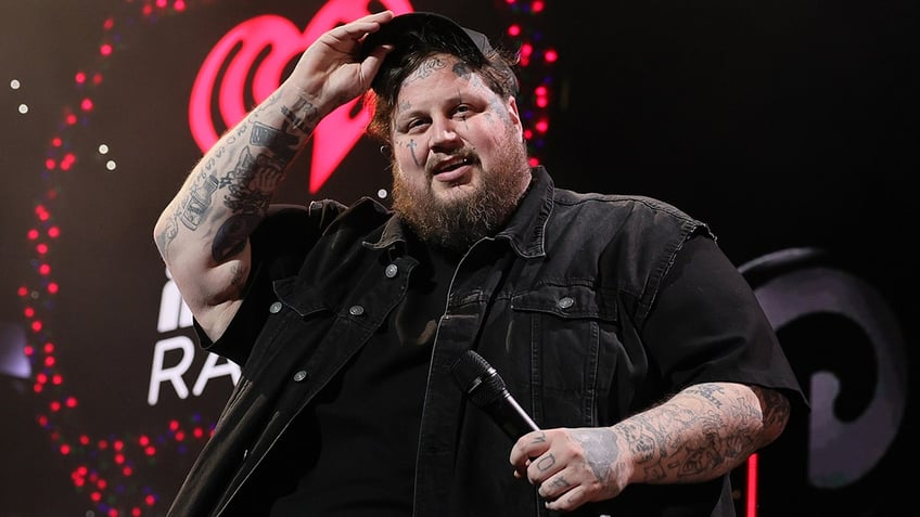 Jelly Roll lifts up his hat a bit from his head while smiling on stage in Philadelphia