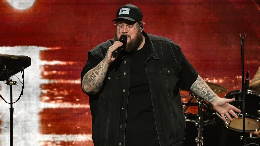 Jelly Roll performs in Philadelphia on stage in a black shirt and black jean vest and black hat