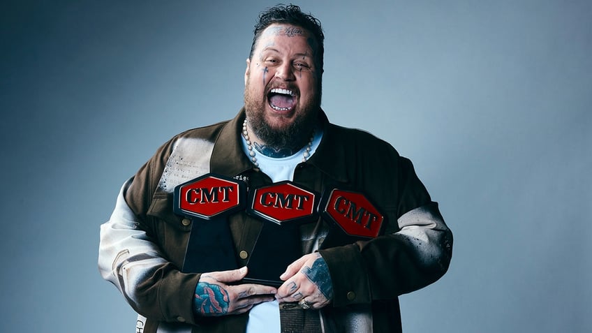 Jelly Roll holds his 3 CMT Awards and smiles really big for the camera