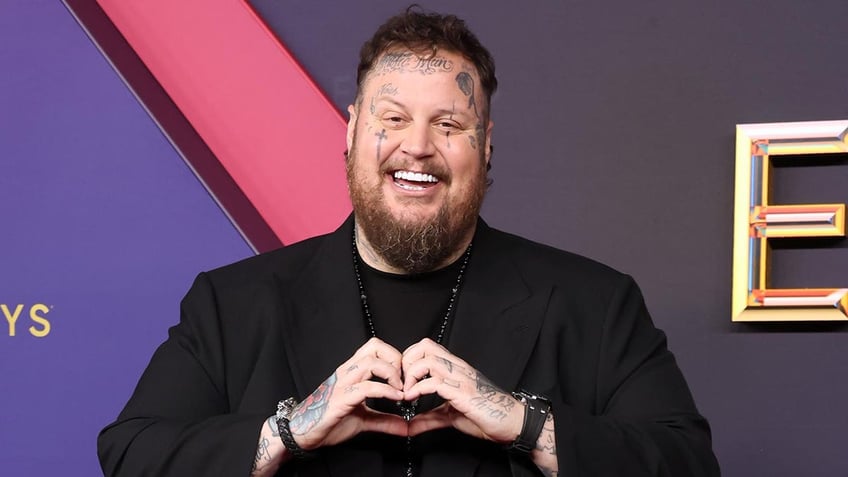 Jelly Roll in a black suit makes a heart with his hands at the Emmy Awards