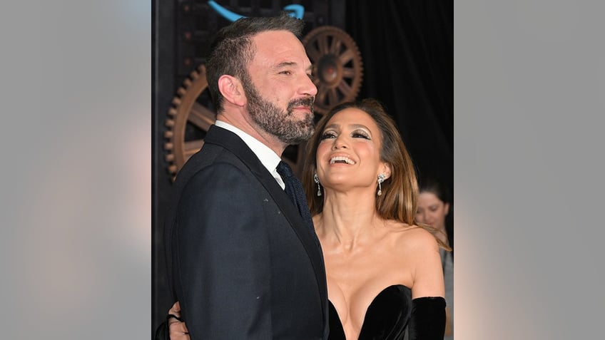 Jennifer Lopez in a strapless black dress looking up and laughing at Ben Affleck in a suit