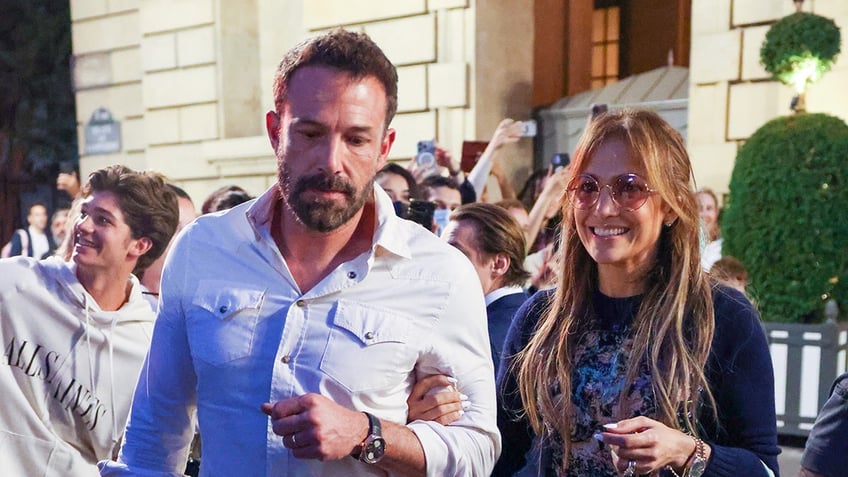 Ben Affleck looking serious with a smiling Jennifer Lopez walking through a public space