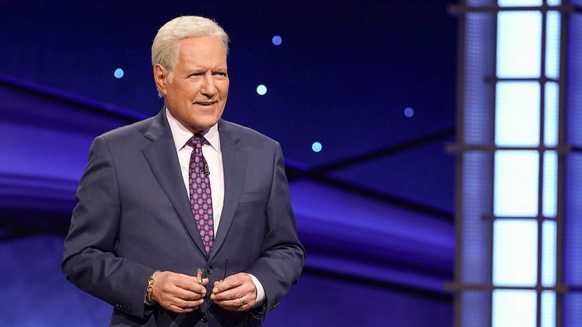 Alex Trebek in a dark suit and purple tie on "Jeopardy"