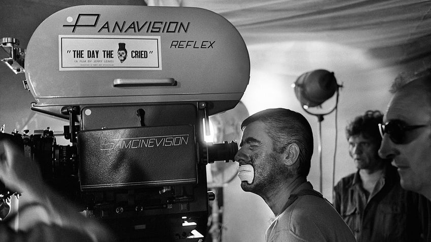 Jerry Lewis dressed as a clown looking through a camera.