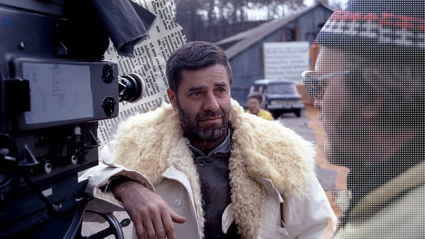 A close-up of Jerry Lewis on set looking serious and wearing a coat.