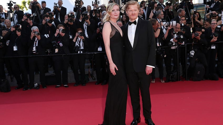 Kirsten Dunst and Jesse Plemons on the red carpet at the 2024 Cannes Film Festival wearing a black dress with a bow in her hair and a black tuxedo.