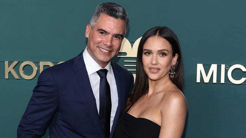 Cash Warren in a navy suit and tie poses next to wife Jessica Alba in a black strapless dress on the carpet