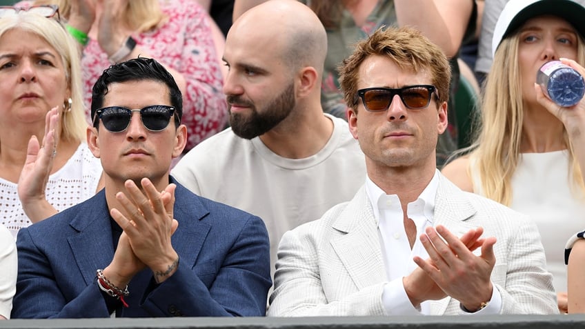 Danny Ramirez and Glenn Powell clap while watching tennis at Wimbledon.