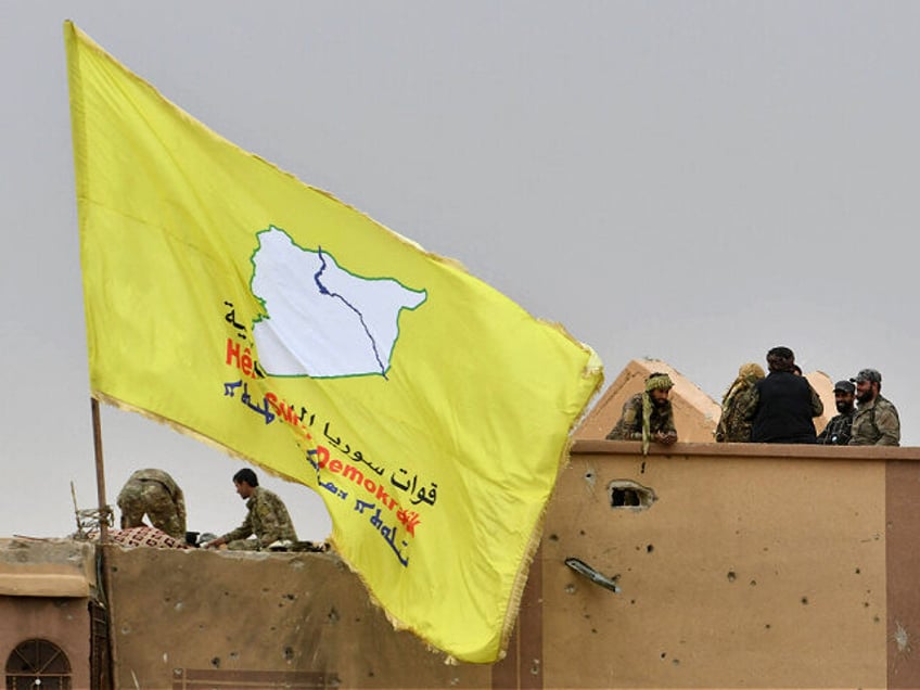 Fighters of the Syrian Democratic Forces (SDF) stand atop a roof next to their unfurled fl