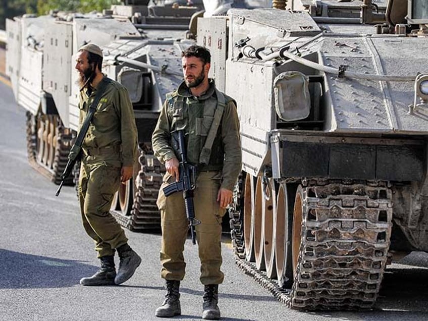 Israeli army soldiers walk before tracked vehicles deployed at a position in the Upper Galilee region in northern Israel near the border with southern Lebanon on October 24, 2023. (Photo by Jalaa MAREY / AFP) (Photo by JALAA MAREY/AFP via Getty Images)