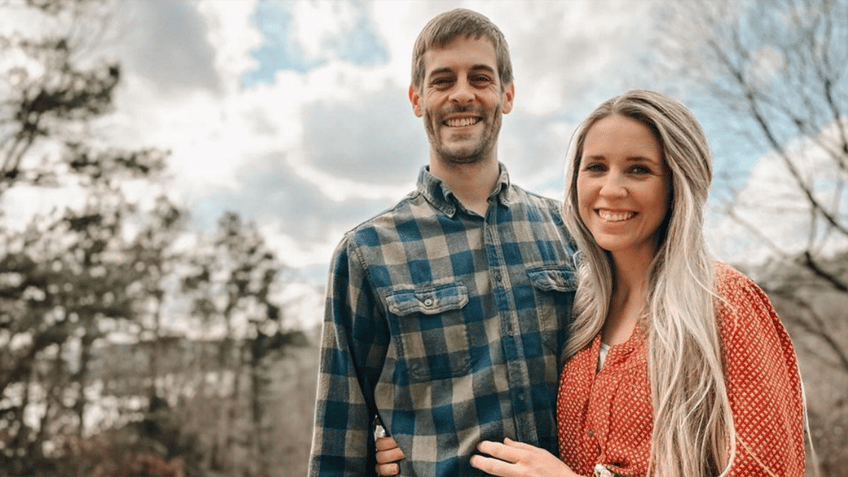 Derick Dillard in a blue plaid shirt smiles with wife Jill Duggar in an orange top 