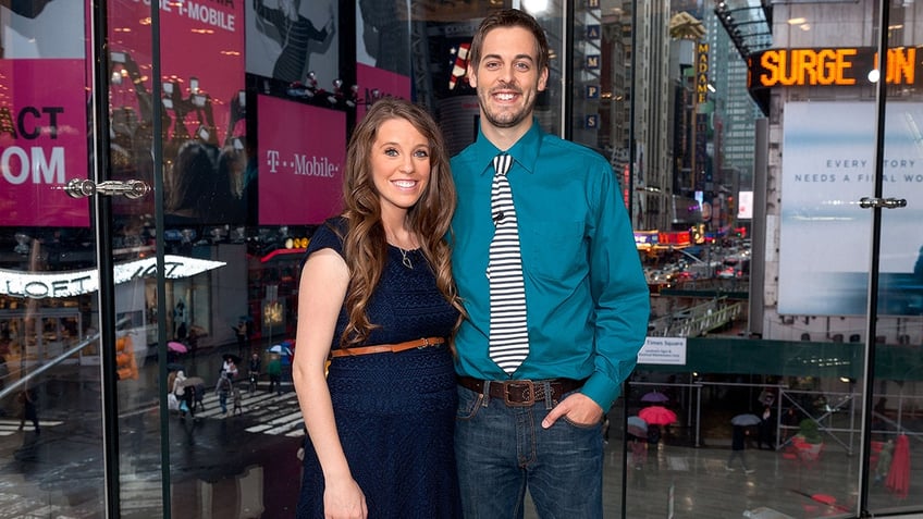 Jill Duggar wearing a sleeveless navy dress standing next to her husband in a teal shirt and striped tie