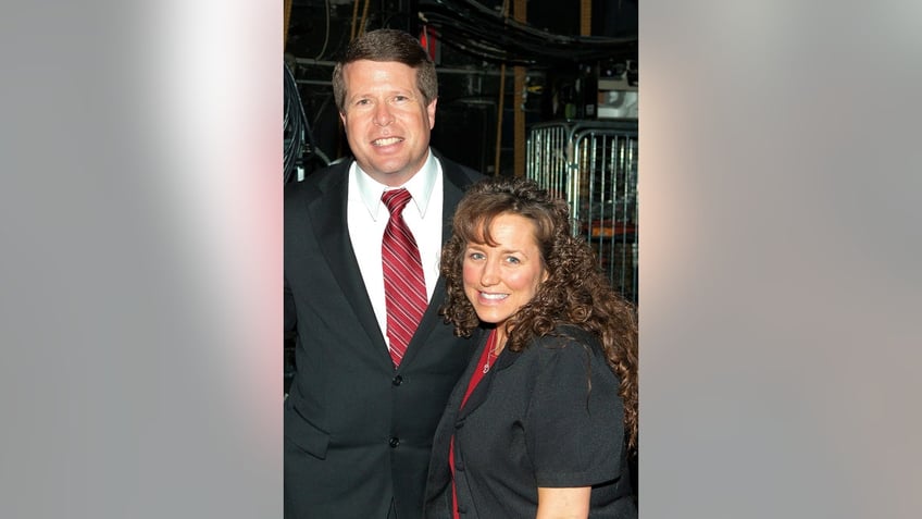 Jim Bob wearing a dark suit and burgundy tie next to his wife Michelle Duggar wearing a black dress