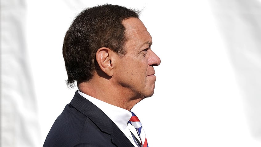 A side profile of Joe Piscopo wearing a suit and a white shirt with a colorful striped tie