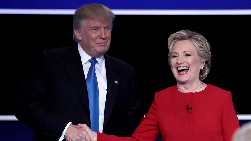 Donald Trump shaking hands with a laughing Hillary Clinton who is wearing a red dress.