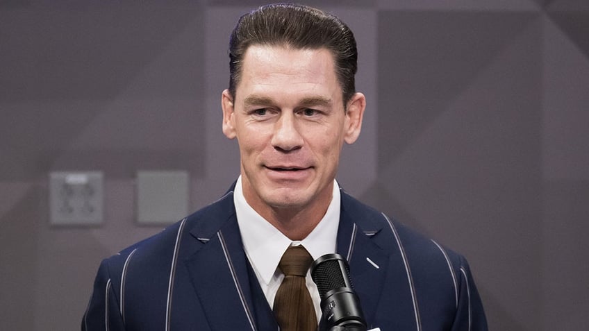 John Cena in a navy striped blazer fends questions from the media