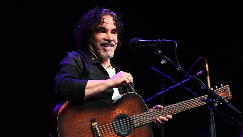 John Oates smiling on stage with a guitar