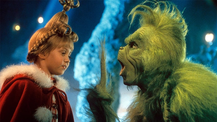 Jim Carrey points his finger as the Grinch towards Taylor Momsen as Cindy Lou, who's wearing a red jacket with wite fur and a braid that stands on her head