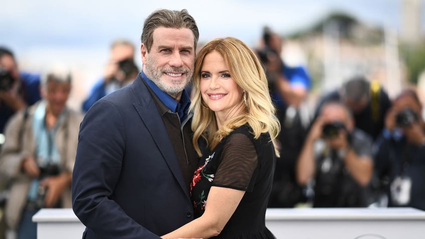 John Travolta hugs his wife Kelly Preston in a black dress on the red carpet