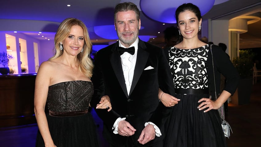 Kelly Preston in a black gown has her arm wrapped around husband's John Travolta in a black tuxedo whose daughter, Ella in a black and white patterned dress holds her fathers arm