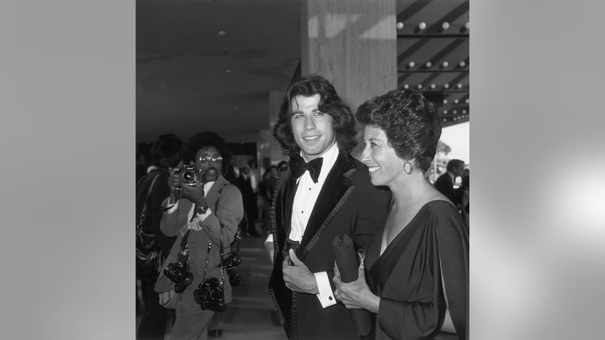 Ellen Travolta and John Travolta walking near a photographer