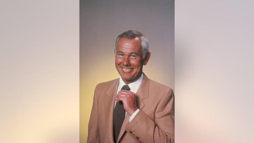 Johnny Carson smiling and adjusting his tie.