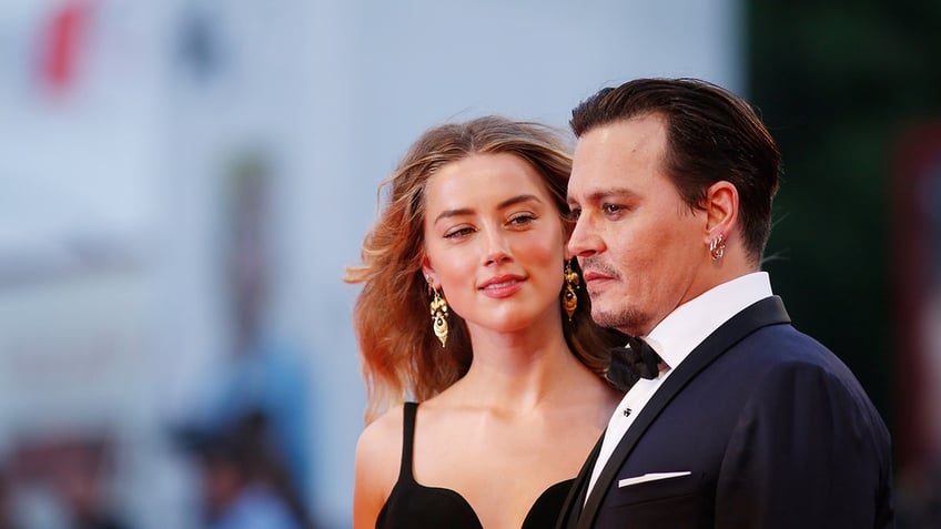 Amber Heard looking at Johnny Depp wearing a black low-cut dress at the red carpet.