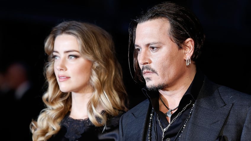 Amber Heard and Johnny Depp looking to the side as they wear matching black outfits.