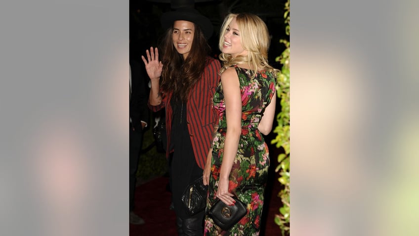 Amber Heard smiling wearing a floral dress outdoors standing really close next to her girlfriend.