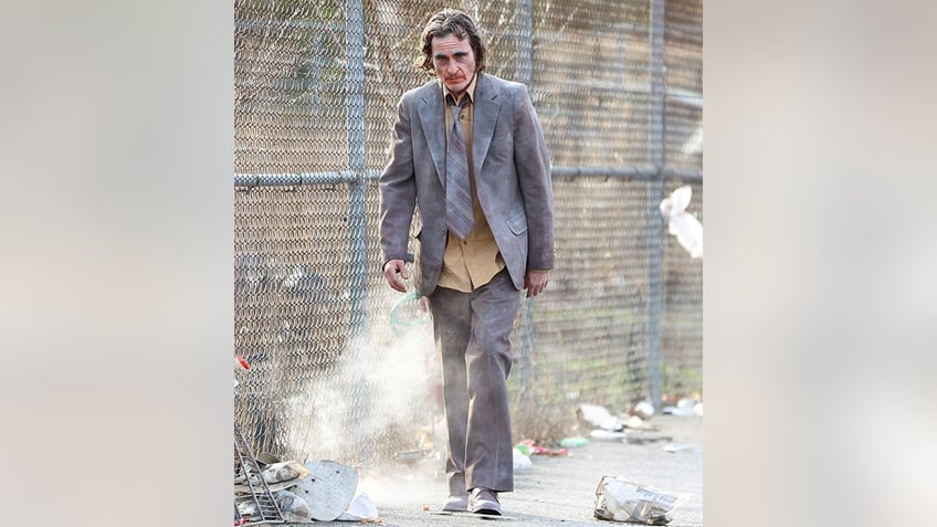 Joaquin Phoenix in character for "Joker: Folie à Deux," wearing a suit with a yellow shirt