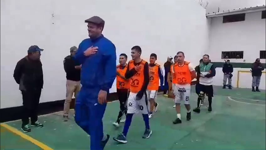 Joran van der Sloot towers over his soccer teammates in a Peru prison, holding his hand over his heart and wearing a blue tracksuit