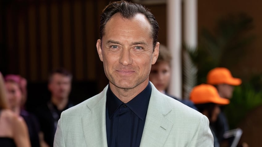 Jude Law wearing a black shirt and gray suit