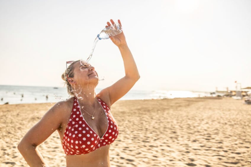A young woman on the beach cools down with cold water during the summer heat.