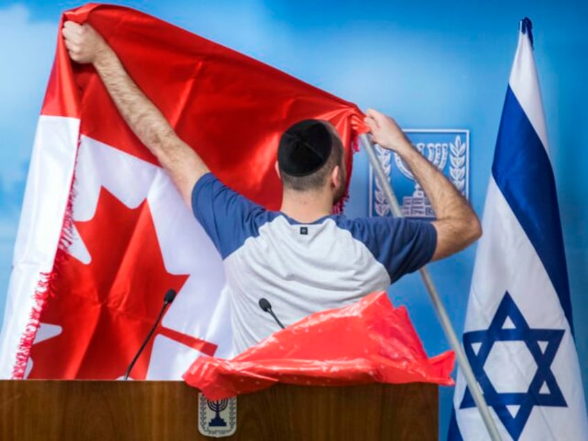 A worker prepares the Canadian flag next to the Israeli flag ahead of the arrival of Canad