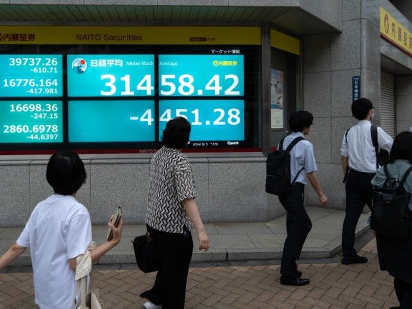 Pedestrians walk past monitors displaying the Nikkei 225 Stock Average figure outside a se