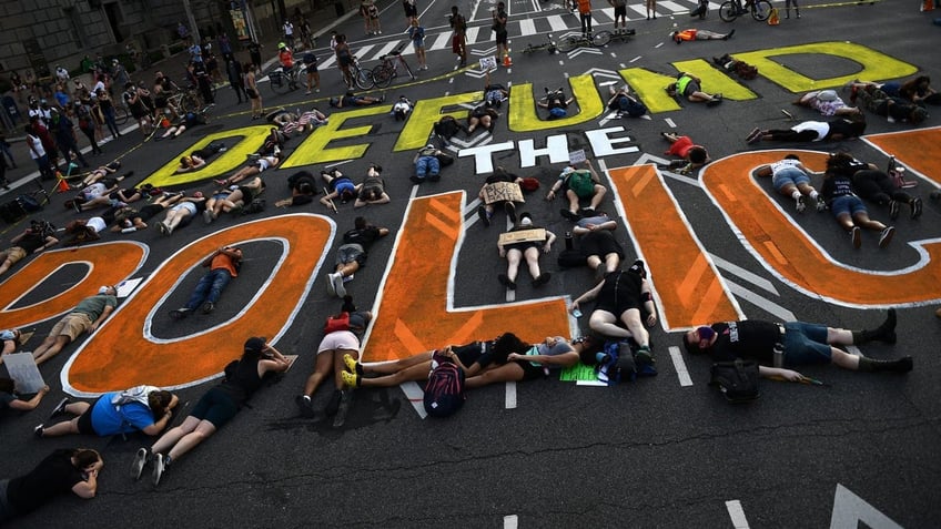 Demonstrators lie on the pavement around letters that say "DEFUND THE POLICE"